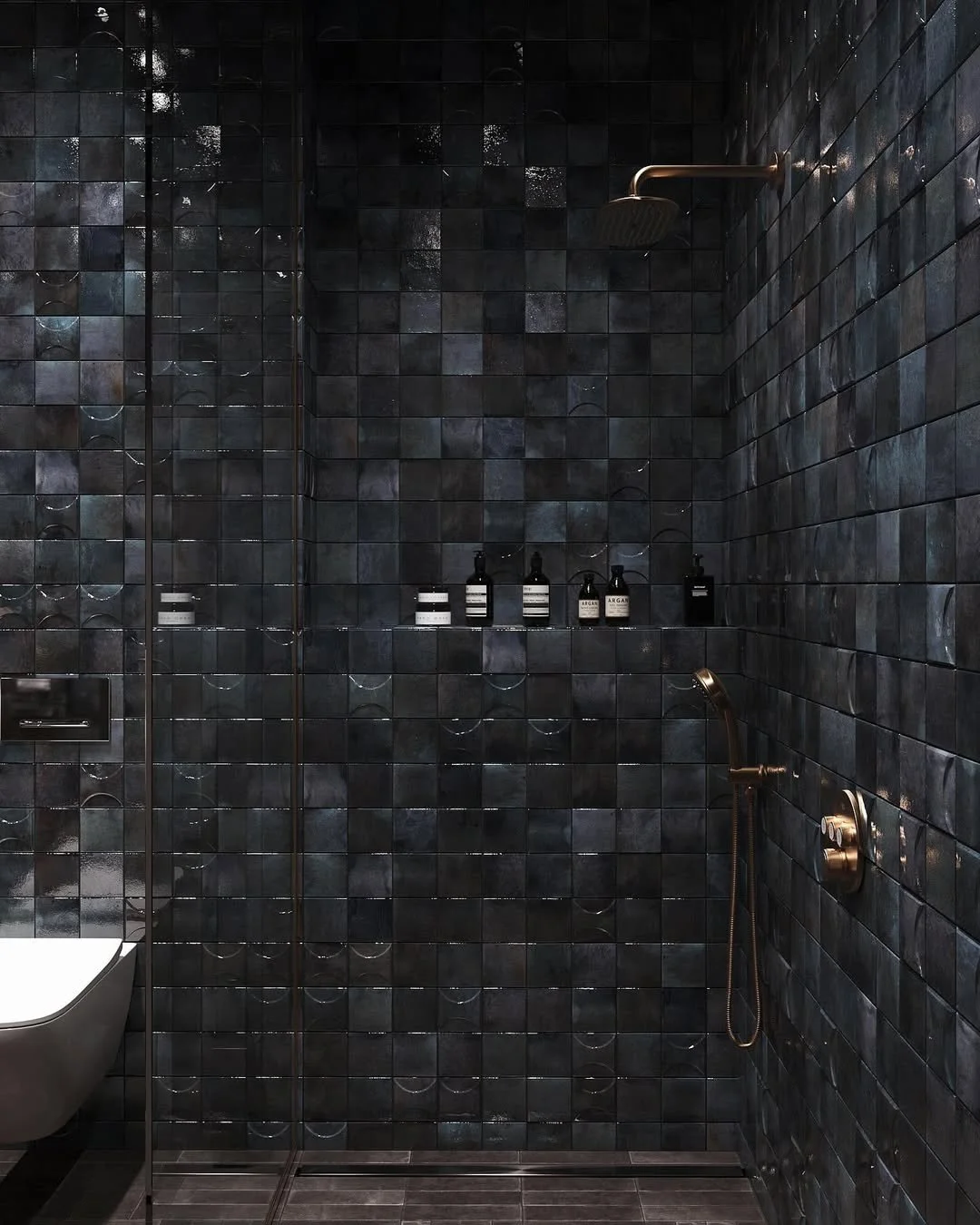 Une douche dans une salle de bain moderne avec des carreaux noirs, un pommeau de douche rond en haut à droite, une autre douchette au mur à droite, et des bouteilles de savon ou shampoing sur une niche intégrée.
