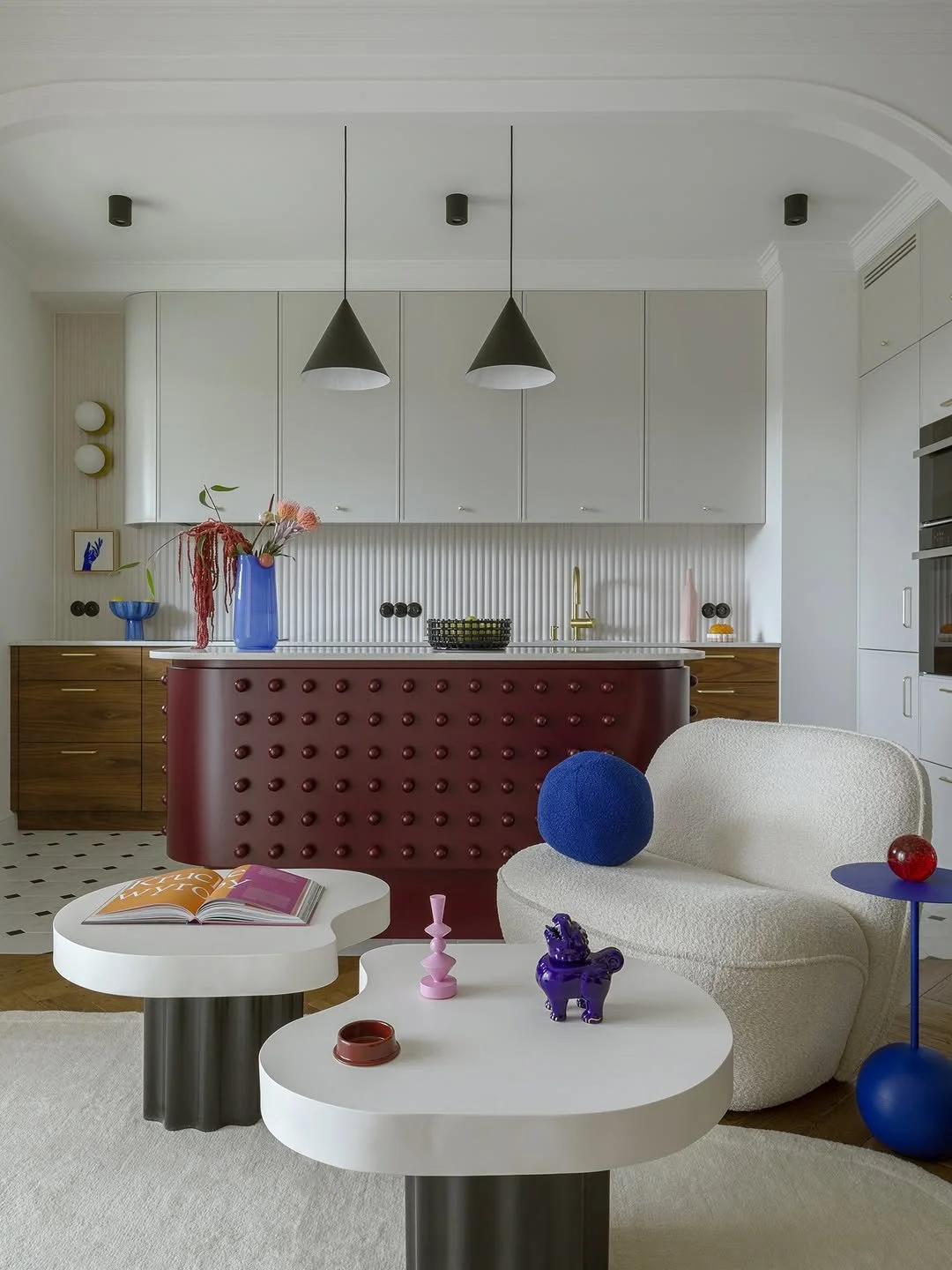 Salon moderne avec meubles blanc, canapés au design arrondi, décor coloré avec accessoires décoratifs en bleu, violet, rouge et pastel, dans un espace lumineux et élégant.