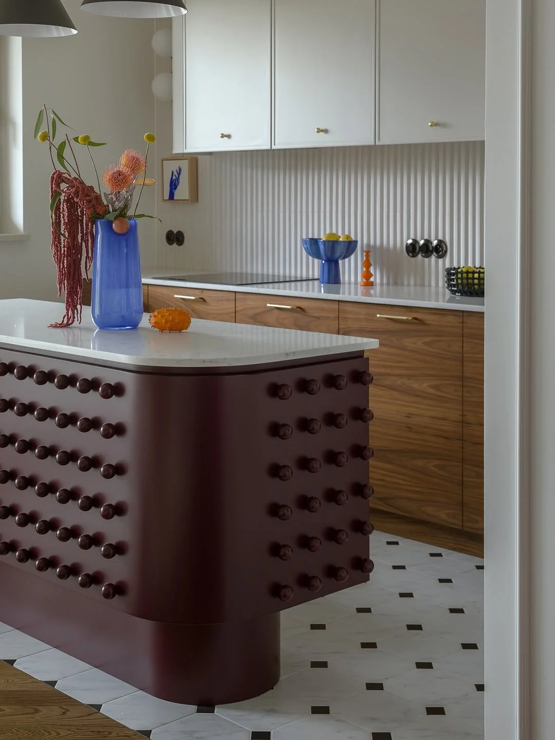 Cuisine moderne avec îlot en bois foncé, placard blanc, et décorations colorées sur le plan de travail, y compris un vase bleu avec des fleurs et un bol azul avec des citrons.