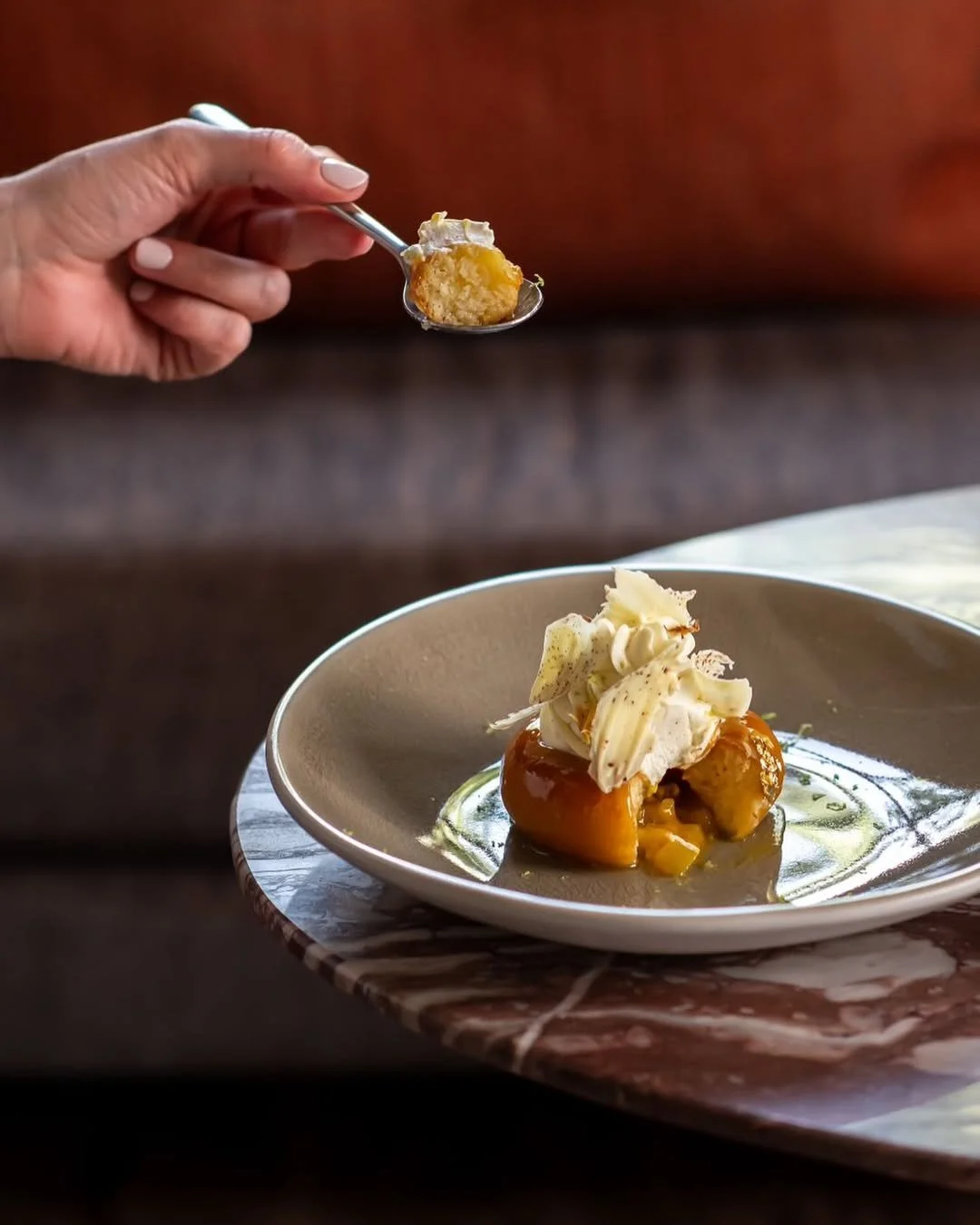 Fois sur une assiette, un dessert avec des morceaux de fruits, de la crème fouettée et une sauce caramel. Une main tient une cuillère avec une bouchée du dessert.