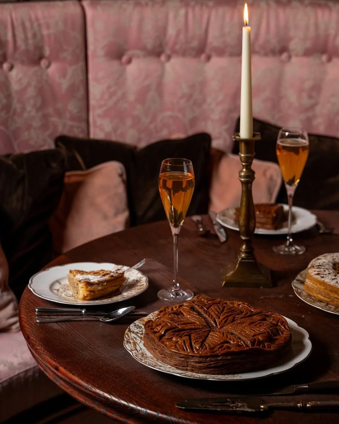 Table avec desserts, deux flûtes de champagne, une bougie allumée, et un vieux canapé en arrière-plan