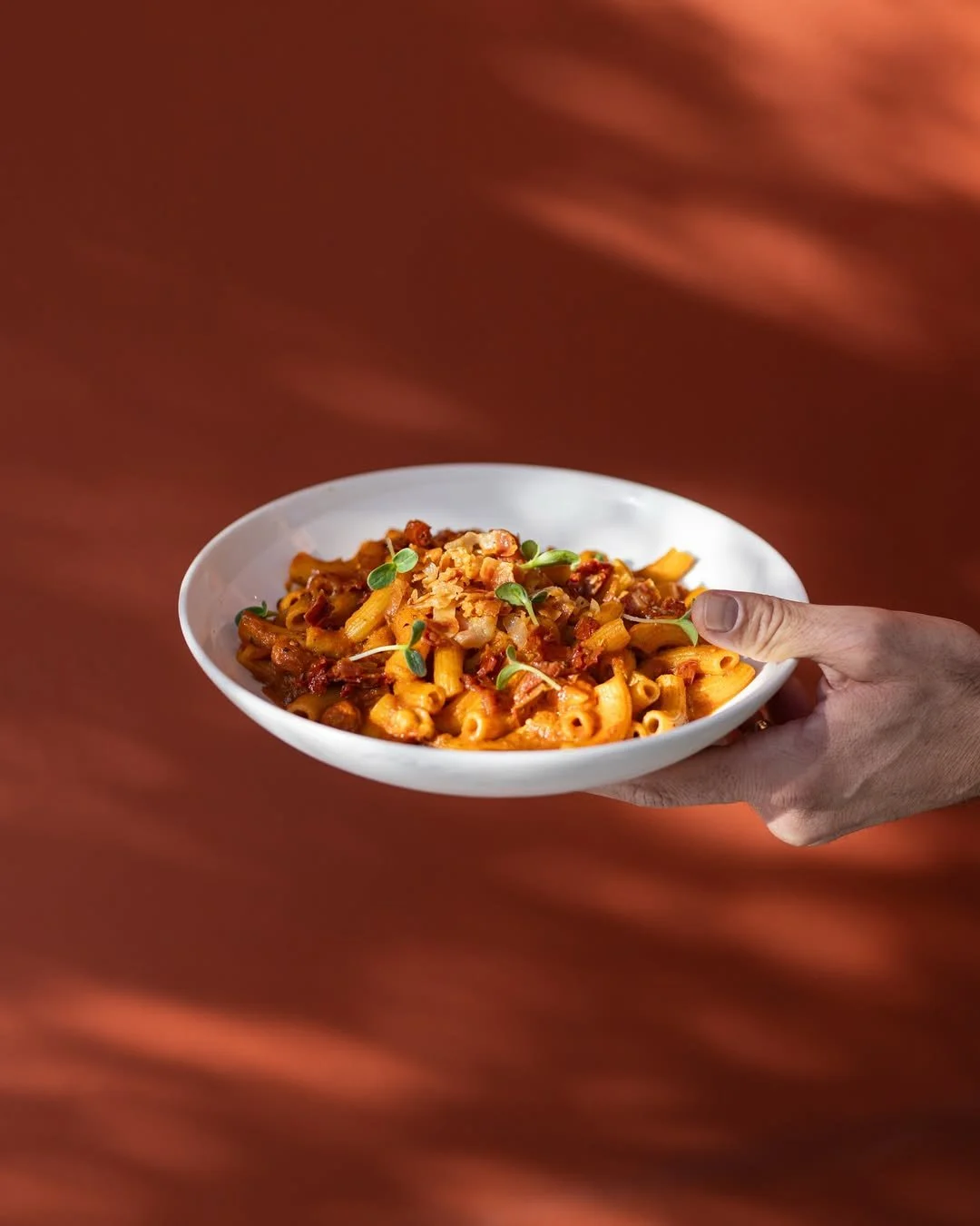 Assiette de pâtes aux sauce tomate avec de la viande hachée, garnie de microgreens, tenue par une main contre un fond en bois