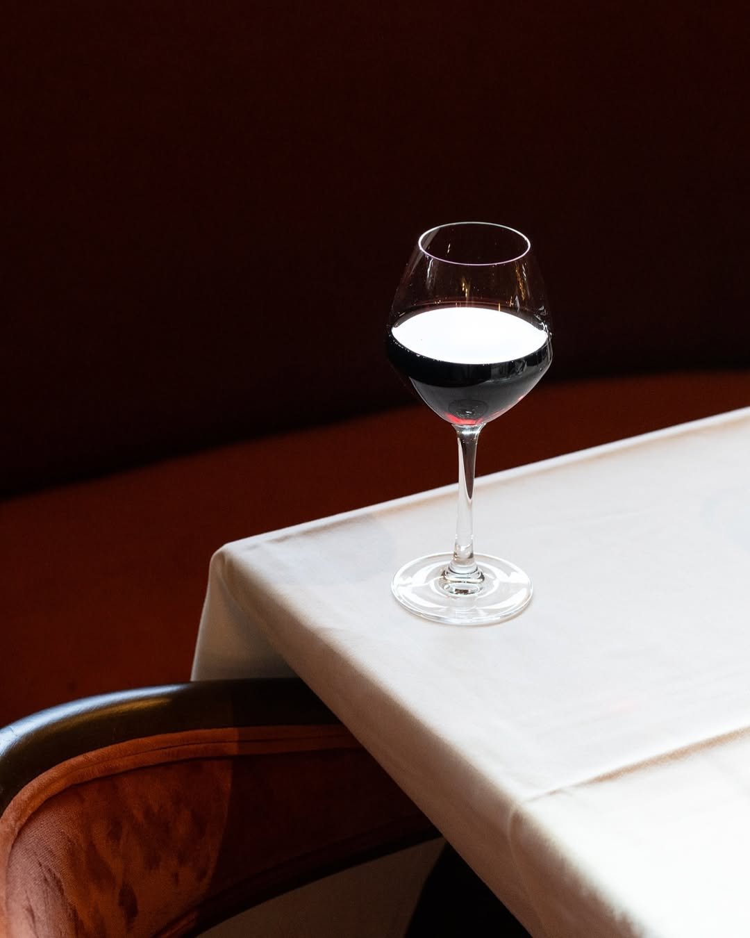 Verre de vin rouge sur une nappe blanche, avec un fond sombre.