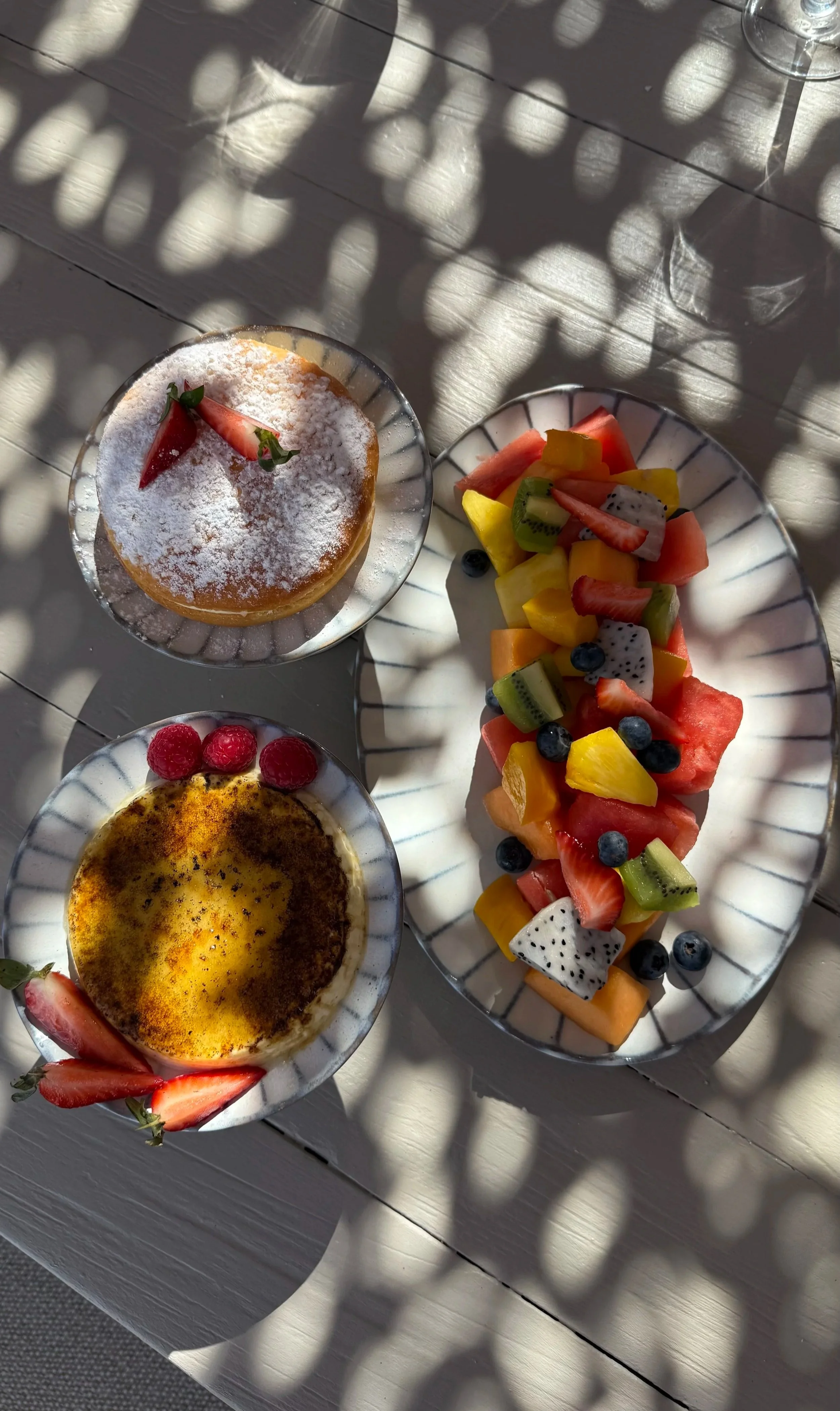 Plateau de fruits frais avec pastèque, kiwi, mangue, papaye, myrtilles, et dragon fruit, accompagné de deux desserts, un avec de la poudre de cacao et fraises, un autre avec de la poudre et des framboises.