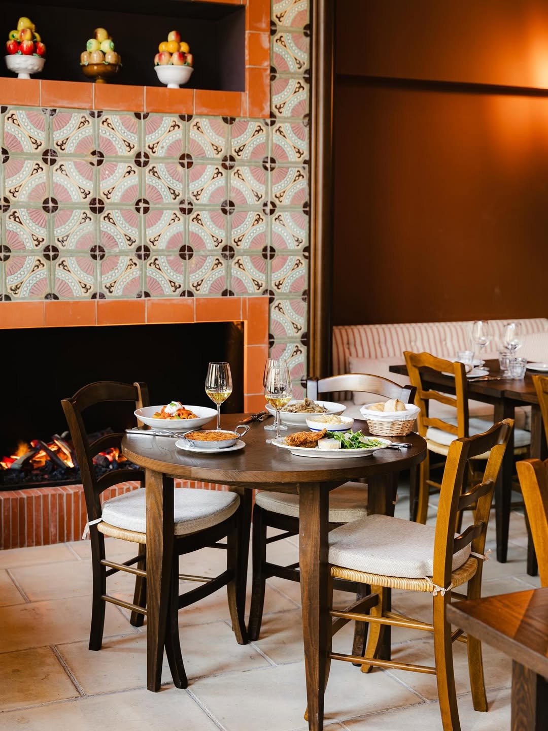 Table de restaurant avec plats, verres de vin, et des assiettes dans un restaurant avec cheminée et murs en tuiles décoratives.
