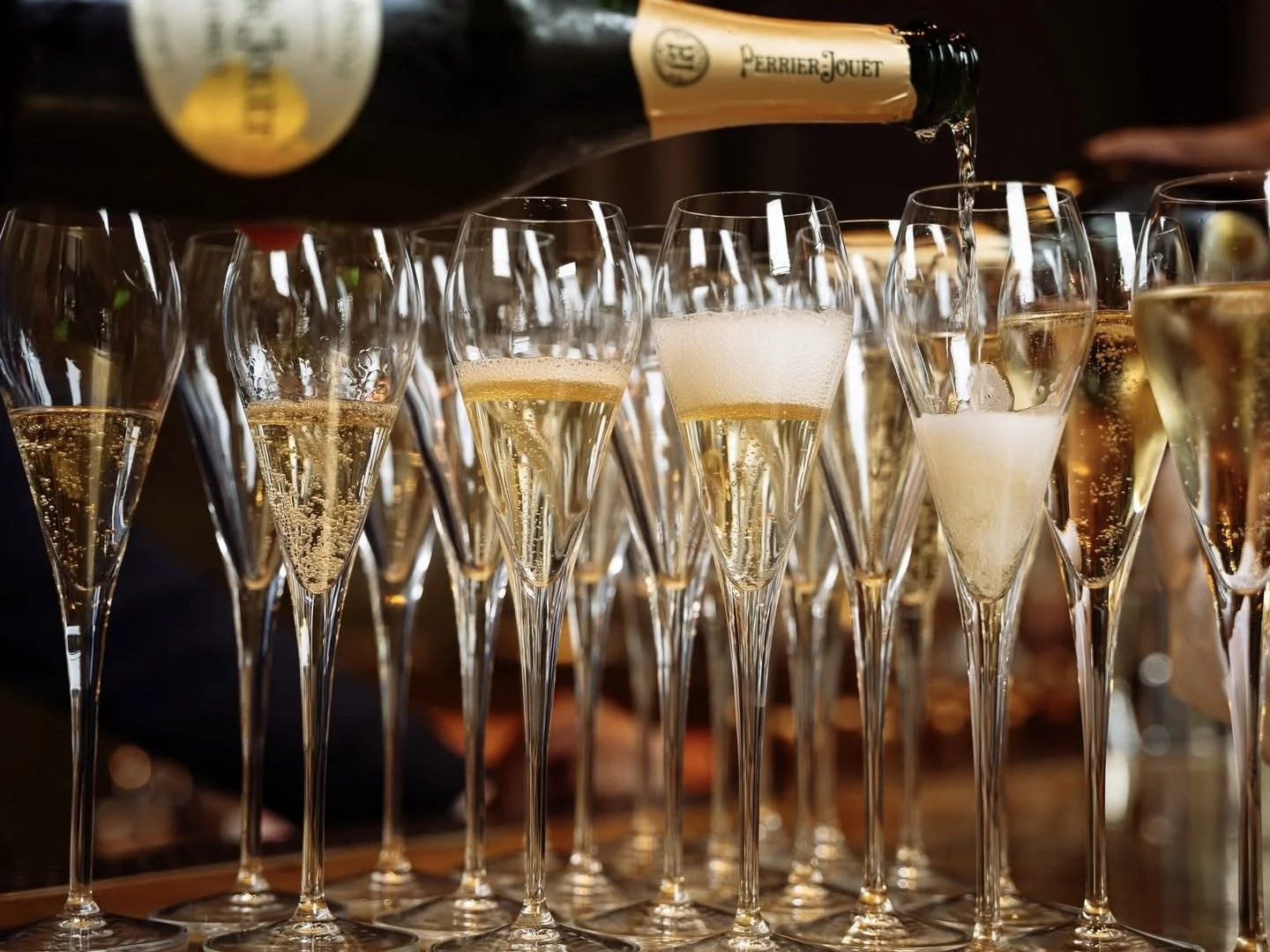 Des flûtes à champagne remplies de champagne étant versé par une bouteille Percy-Jouet.