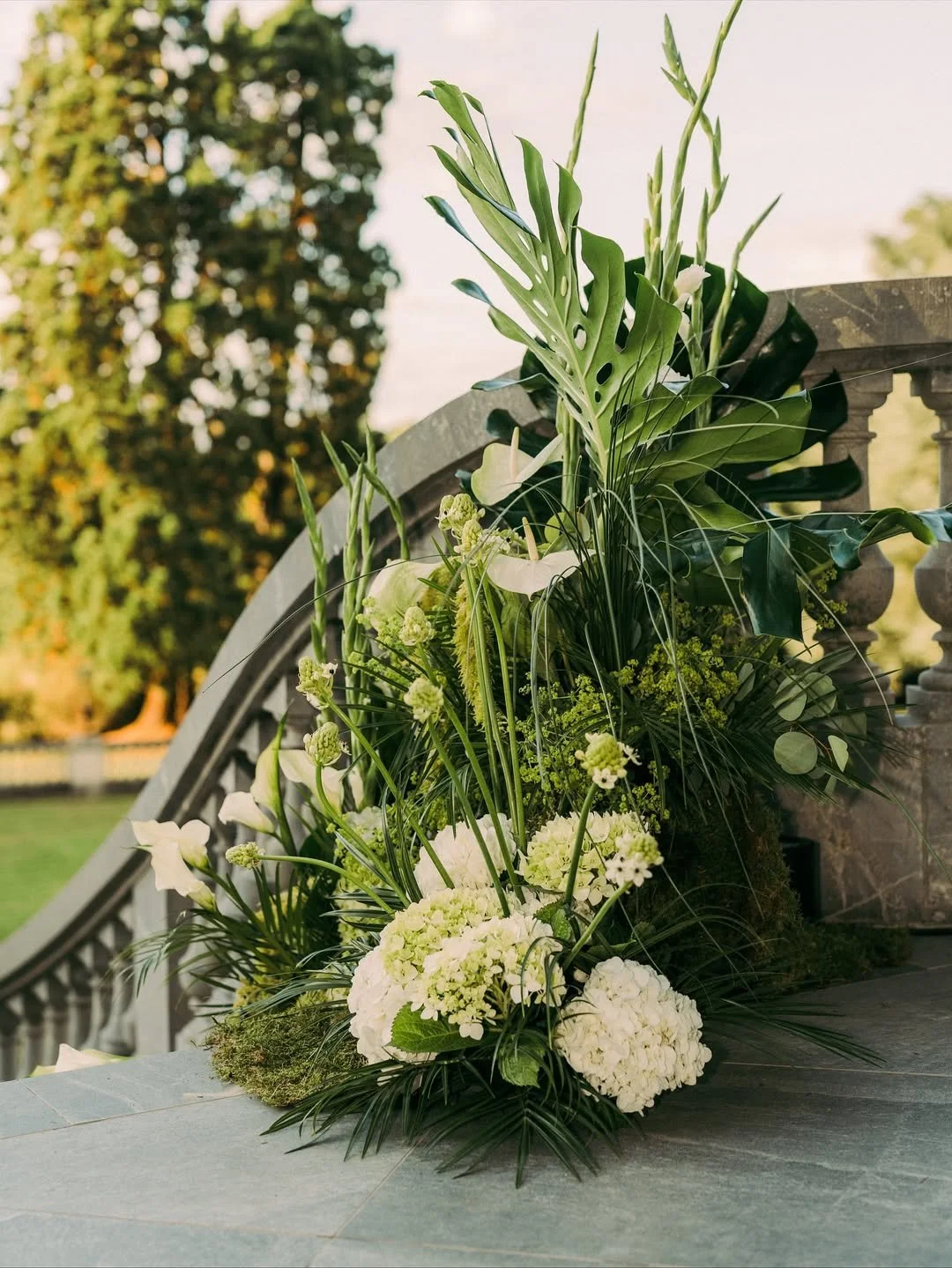 Arrangement floral blanc avec des feuilles vertes, placé sur une surface en pierre.
