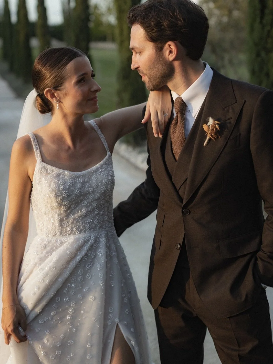 Un couple de mariés en costume et robe de mariage, se regardant tendrement lors de leur mariage en plein air.