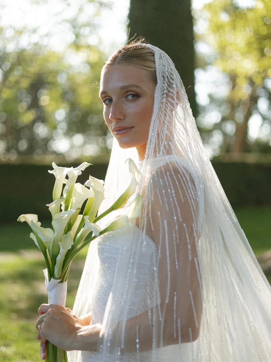 Jeune femme en robe de mariage avec voile, tenant un bouquet de calla lilies, dans un parc en plein air