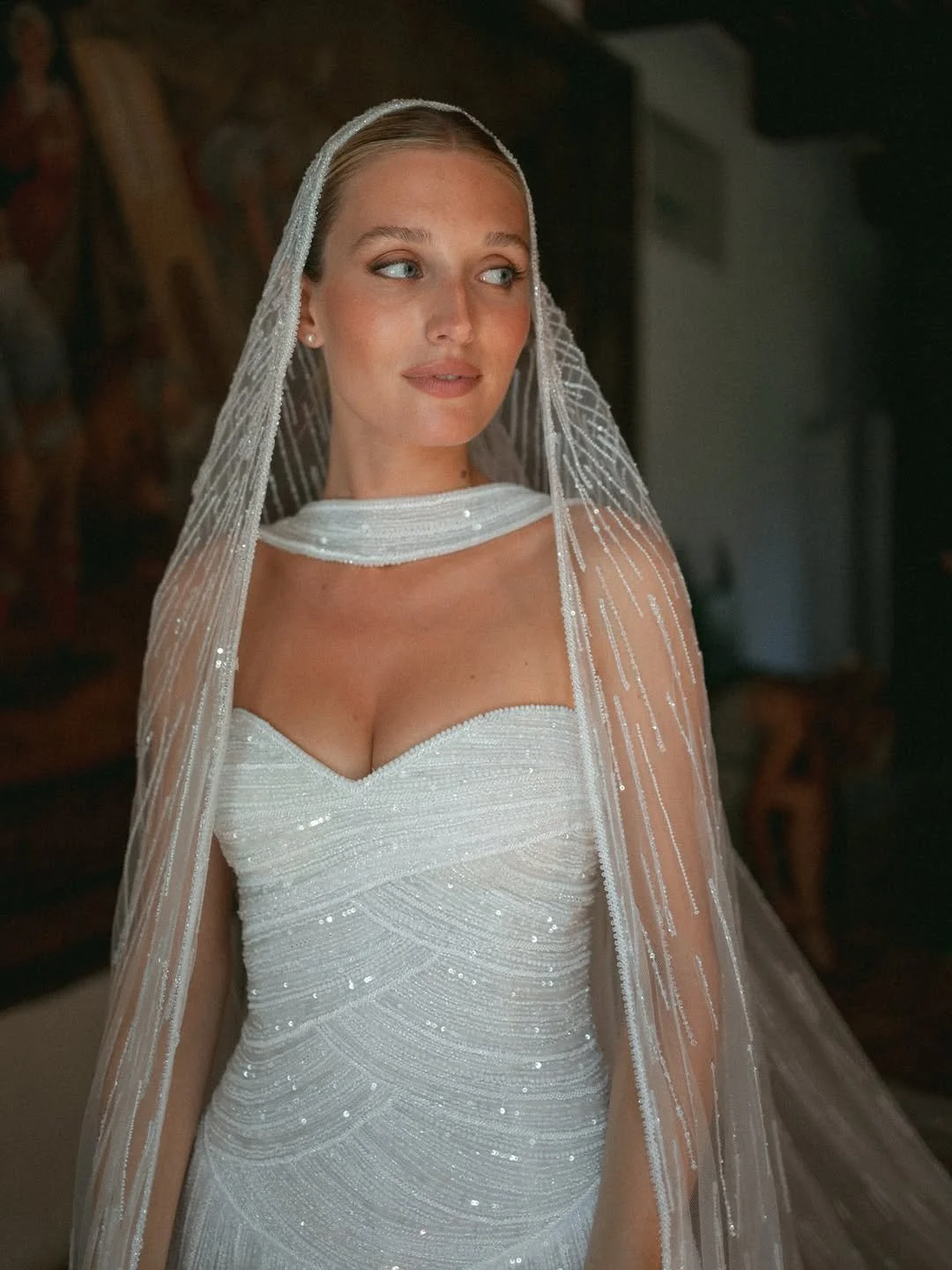 Femme portant une robe de mariée blanche avec un voile ornée de décoration scintillante.