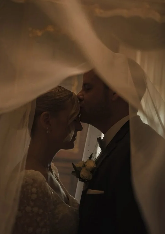 Un couple de mariés en silhouette sous un voile de mariée, partageant un moment intime pendant leur mariage.
