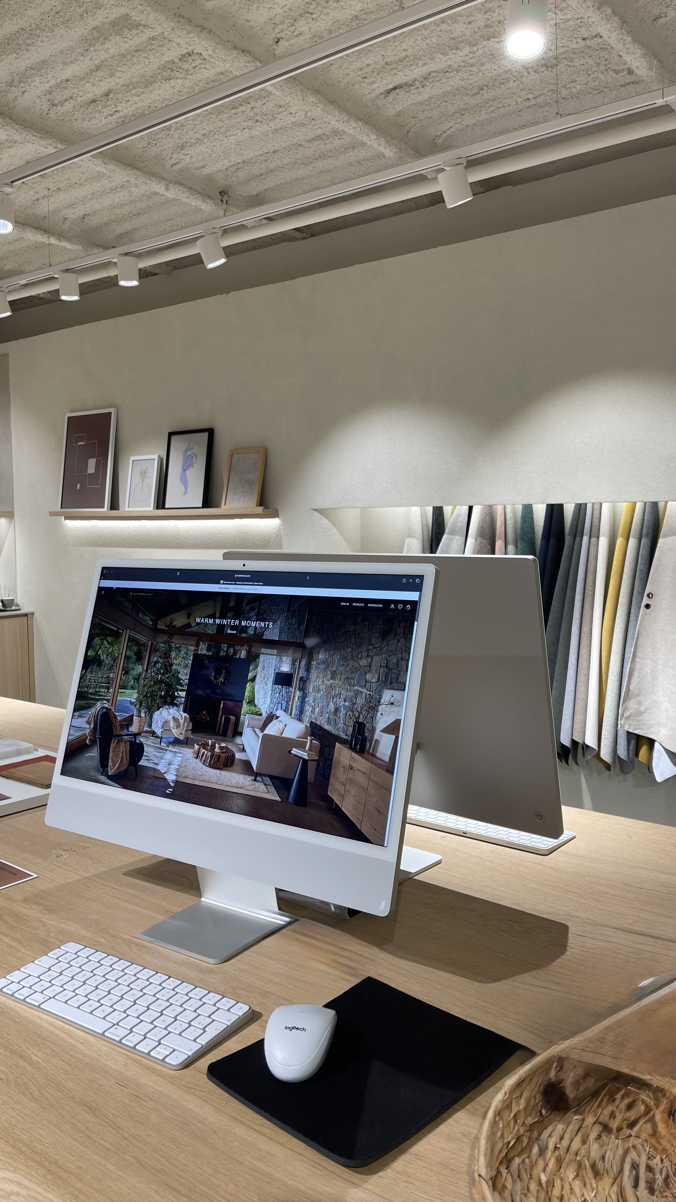 Un ordinateur Apple avec un clavier et une souris Logitech, affichant une image d'un intérieur chaleureux avec un canapé et une cheminée en pierre.