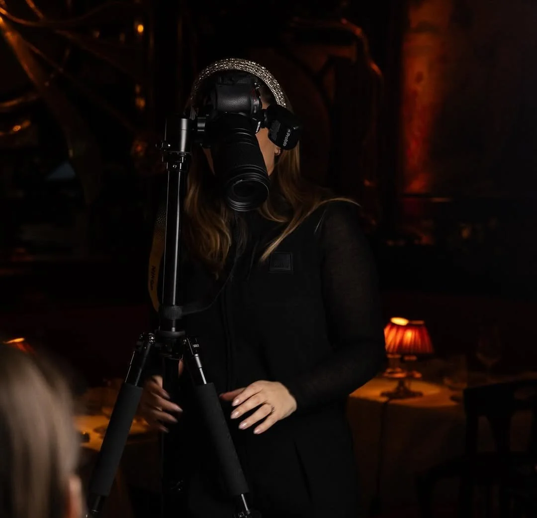 Femme utilisant un appareil photo dans un environnement sombre avec un éclairage tamisé, probablement lors d'une séance photo ou évènement.