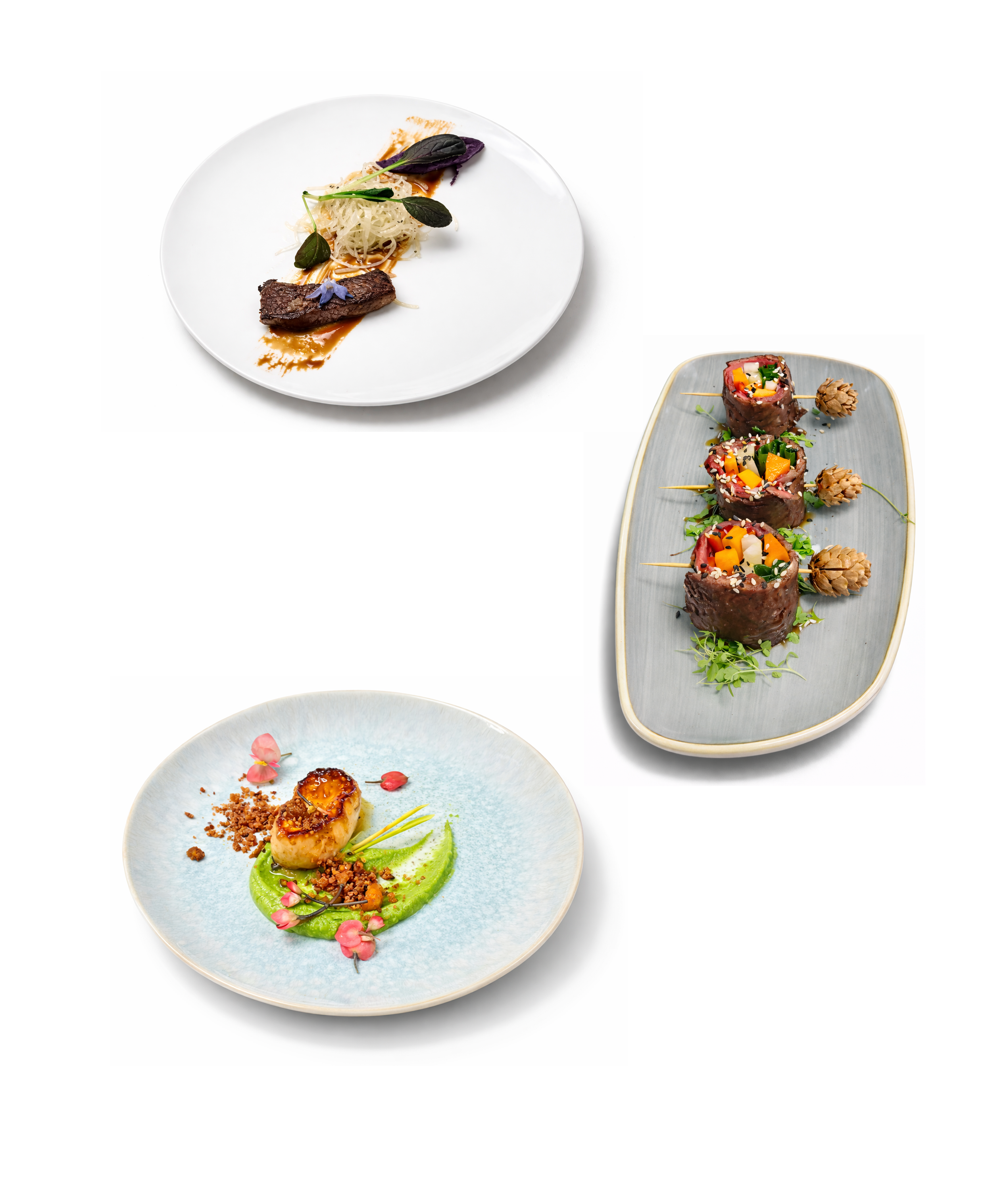 Three plates of gourmet food: a white plate with a piece of steak, shredded vegetables, and greens; a gray plate with three sushi rolls garnished with herbs and seeds; and a light blue plate with a seared scallop, green purée, edible flowers, and crumbs.