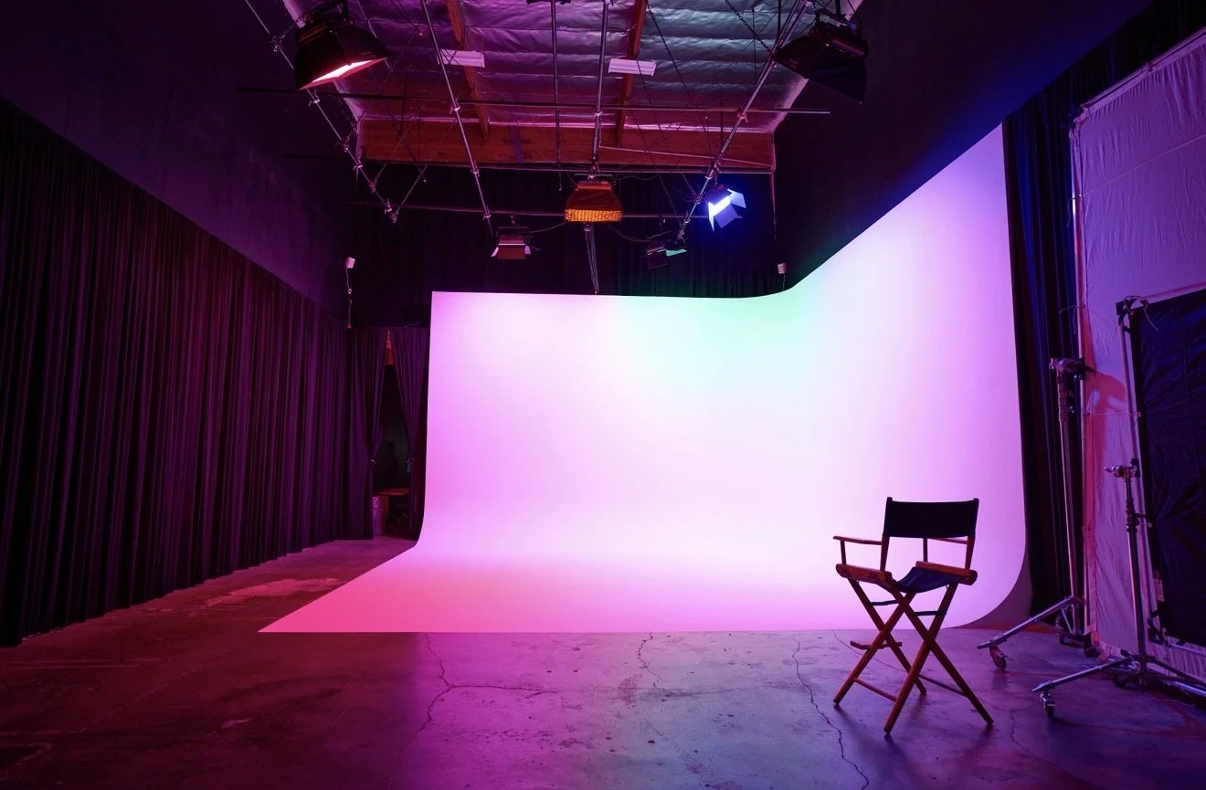Photography studio with a pink and purple gradient backdrop, a director's chair, and studio lighting equipment in a dimly lit room.