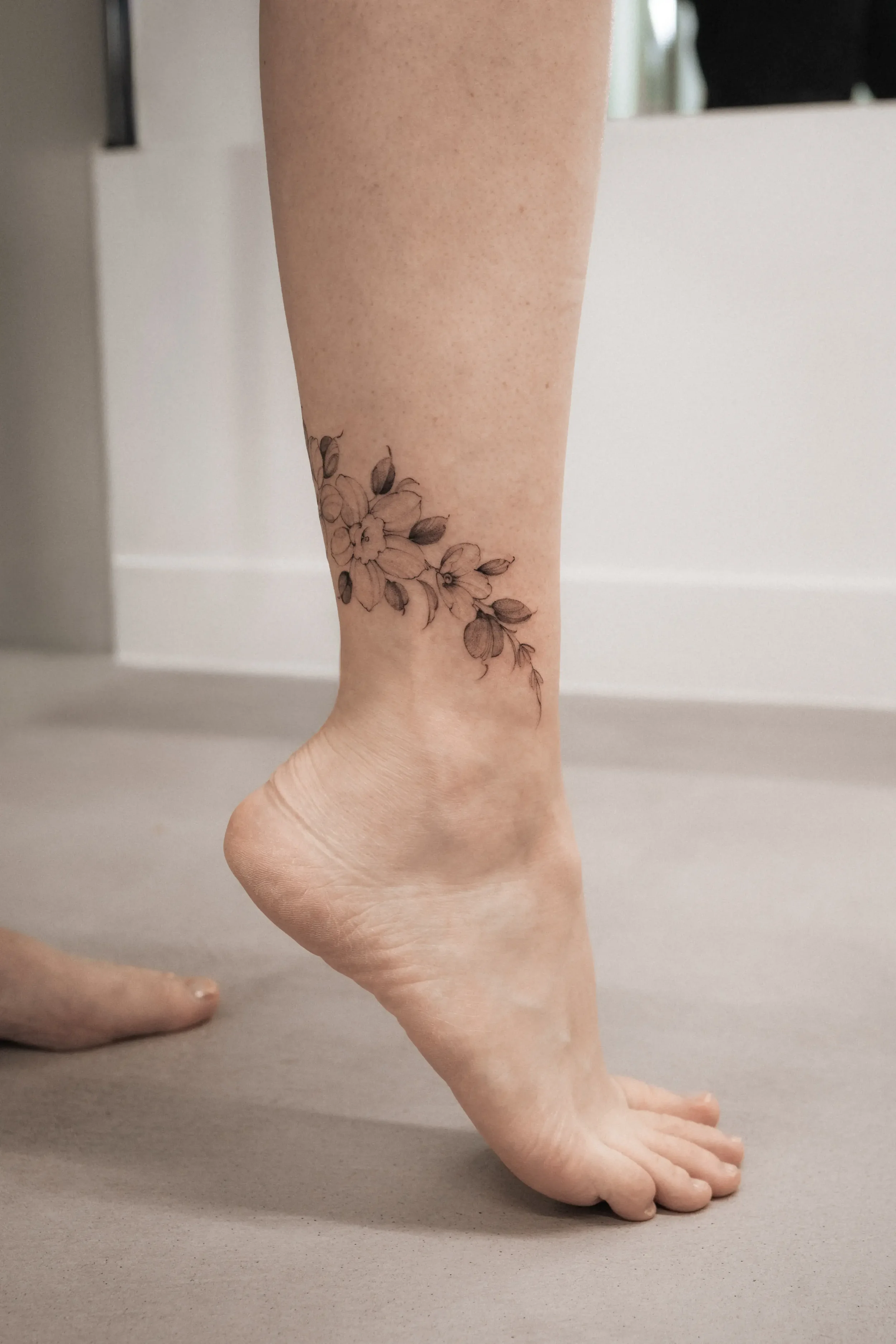 A person's foot and hand on a flat surface, with a floral tattoo on the lower leg