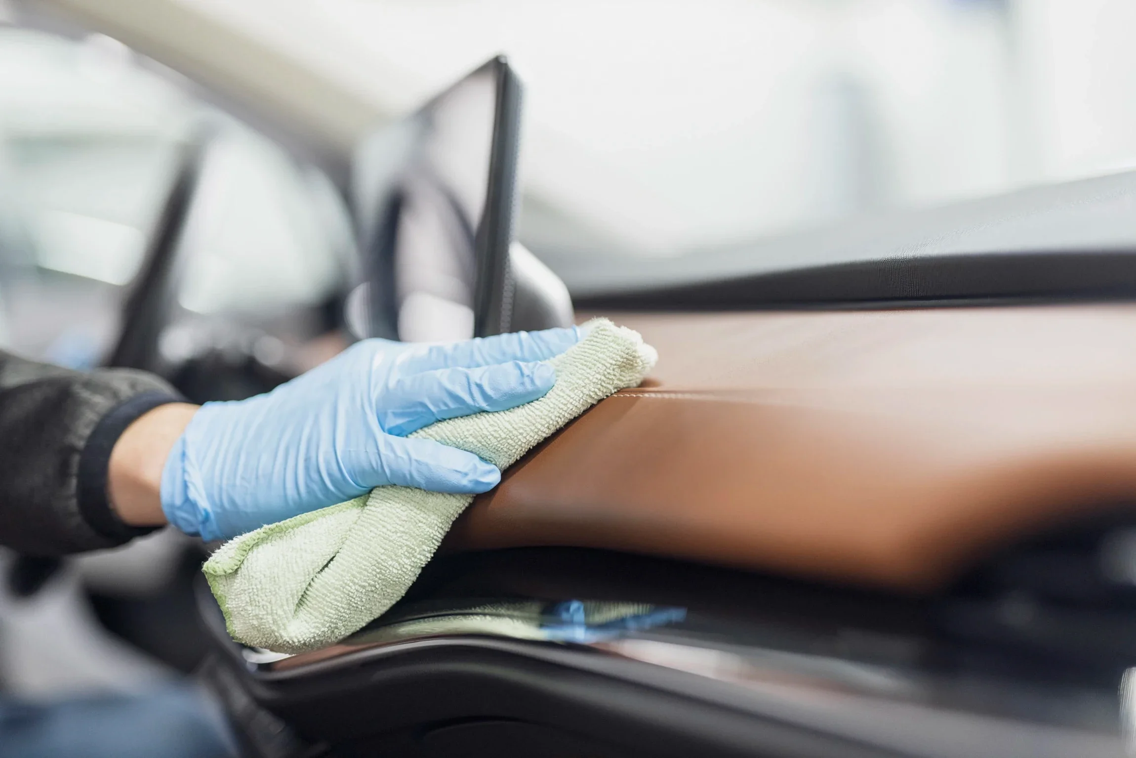 Person wearing a blue glove using a cloth to clean or polish a brown surface inside a vehicle.