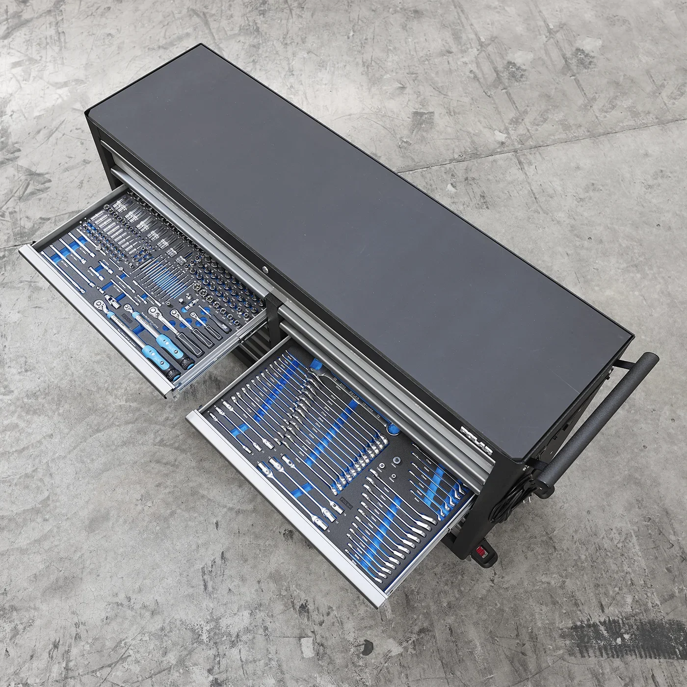 A black toolbox with two open drawers filled with blue and silver hand tools on a concrete floor.