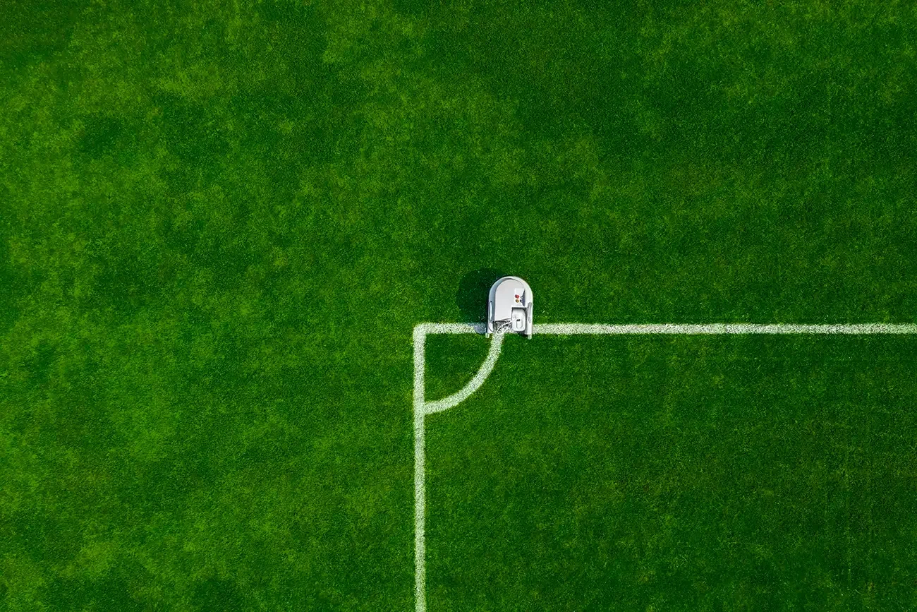 A drone on a soccer field near the corner arc, with white boundary lines on green grass.