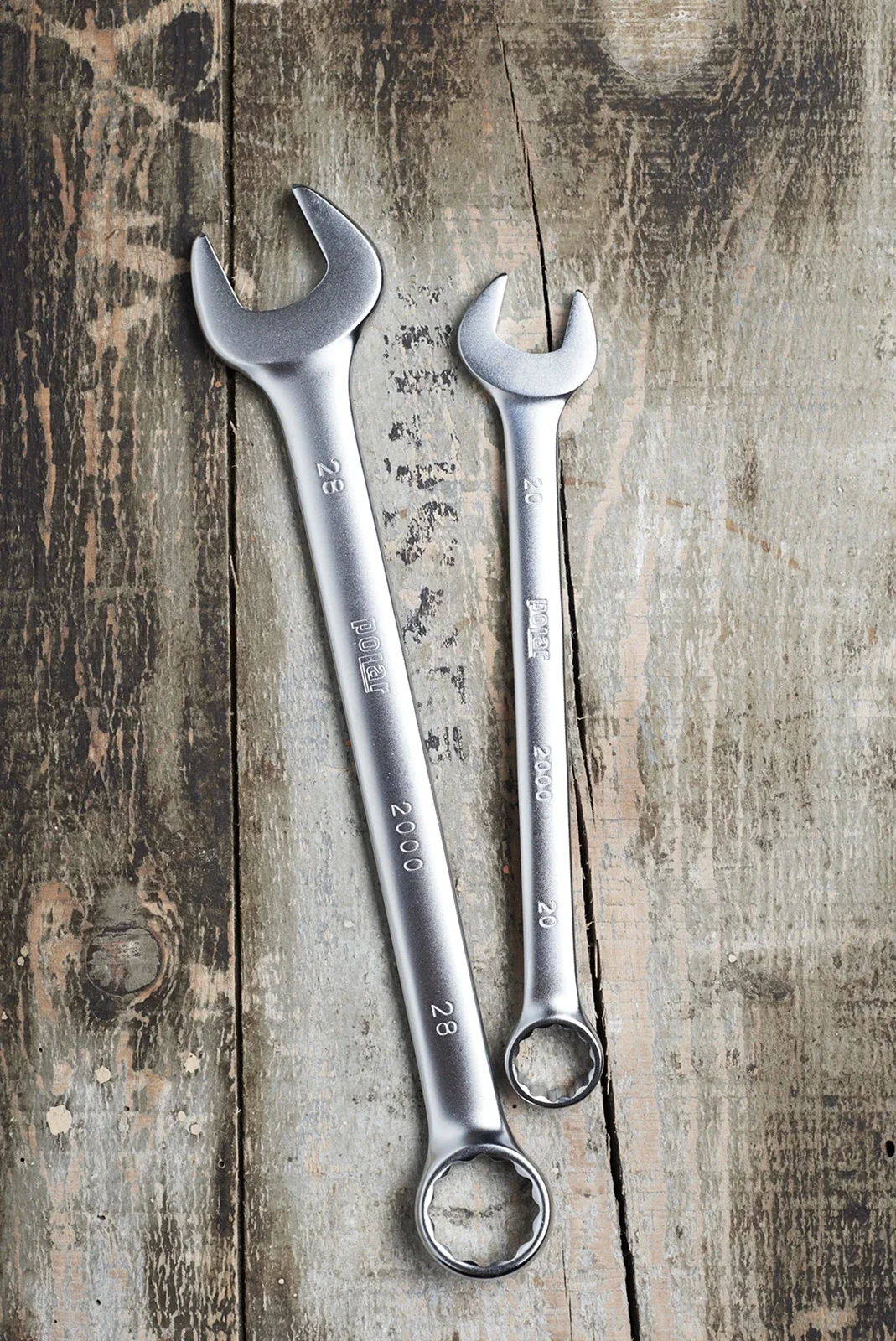 Two metal open-end wrenches on a wood surface, one smaller than the other, both labeled with size and brand.
