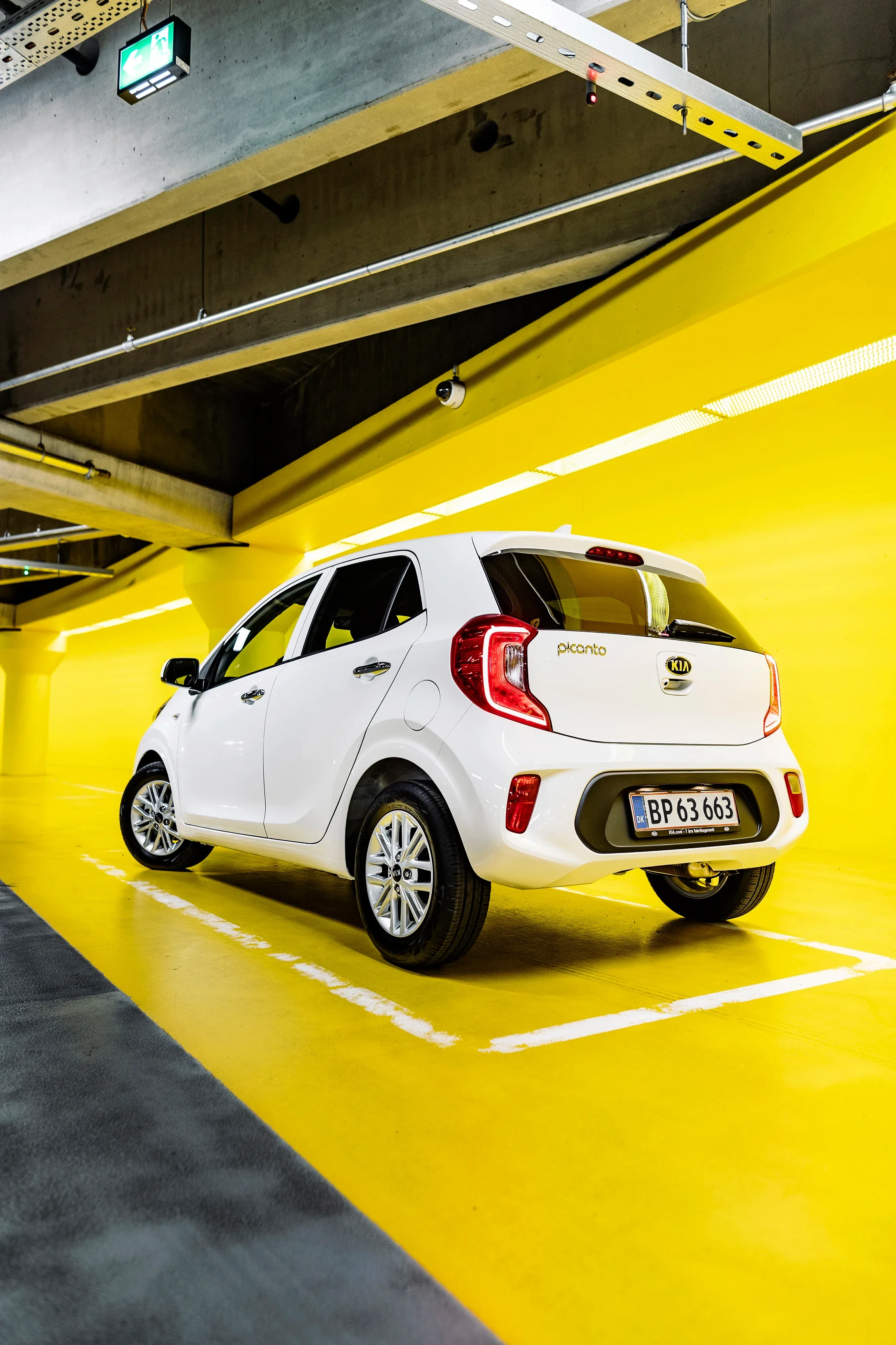 A white Kia Picanto parked in a yellow indoor parking space.