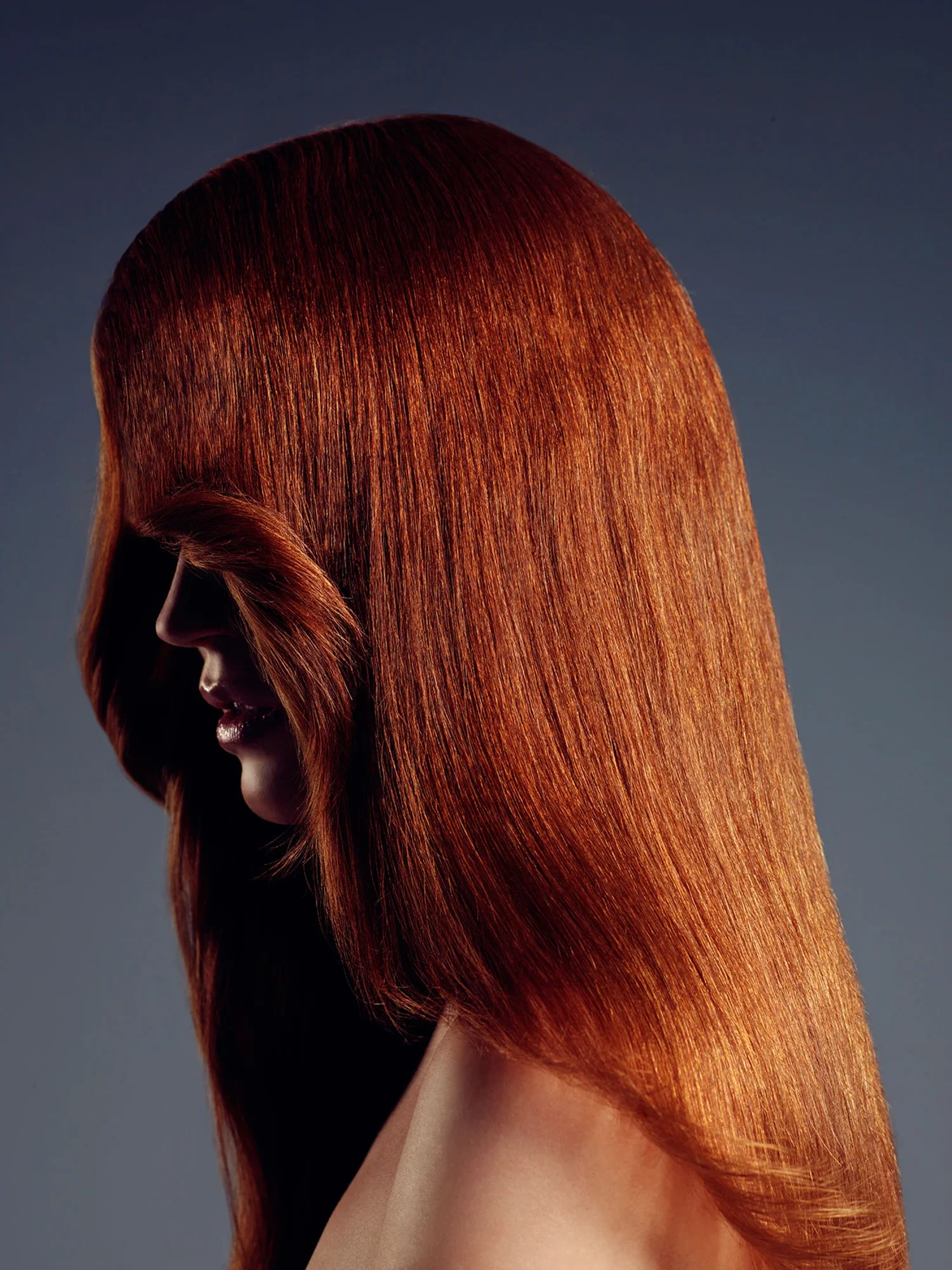 Side profile of a woman with long, straight, vibrant red hair covering part of her face.