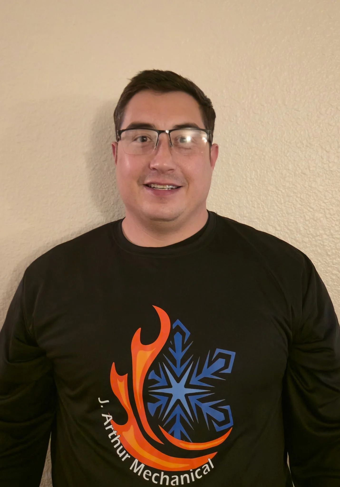 A middle-aged man with gray hair sitting on a beige cushioned bench against a neutral wall, wearing a blue short-sleeved sweater and beige pants, looking to the side.