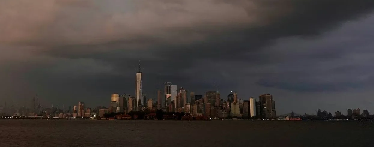 Dark storm clouds looming over the Lower Manhattan skyline at dusk, viewed across the harbor.