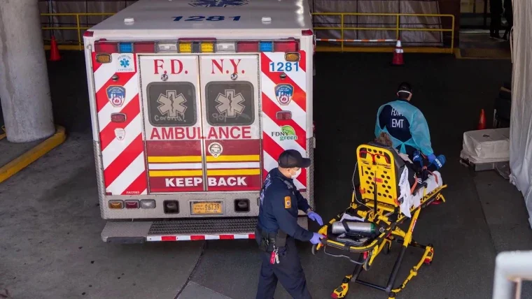 Emergency medical personnel preparing a stretcher outside an ambulance at a hospital or medical facility entrance.