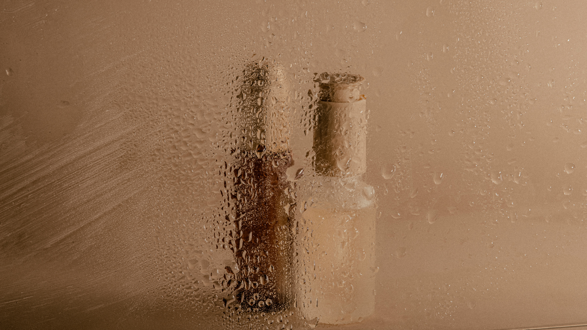 A glass shower door covered in condensation with two bottles of shampoo or body wash inside the shower.