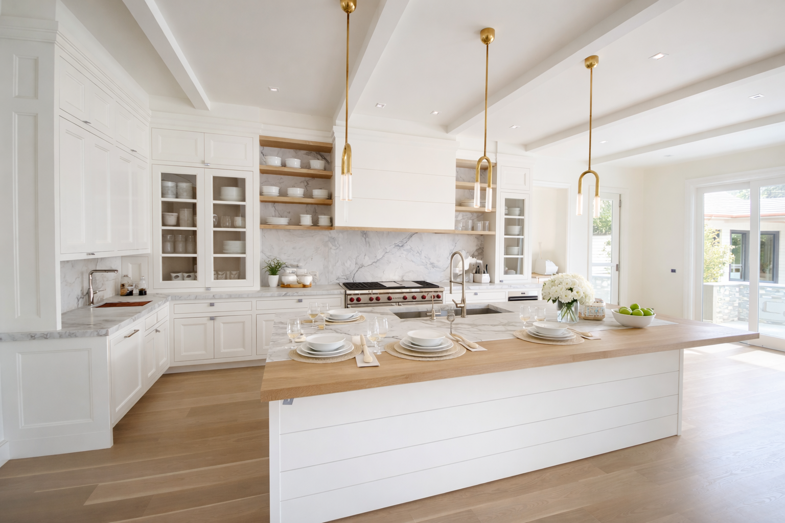 Modern kitchen with white cabinets, marble countertops, and a wooden island with place settings, hanging pendant lights, and large windows letting in natural light.