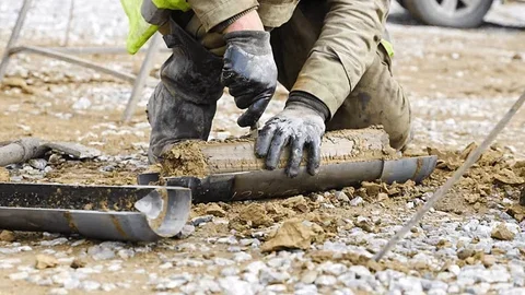 Construction worker installing or repairing underground piping or conduit on a dirt and gravel surface.