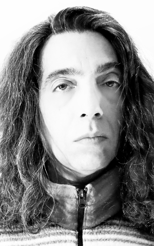 Black and white portrait of a person with long, curly hair wearing a zip-up sweater.