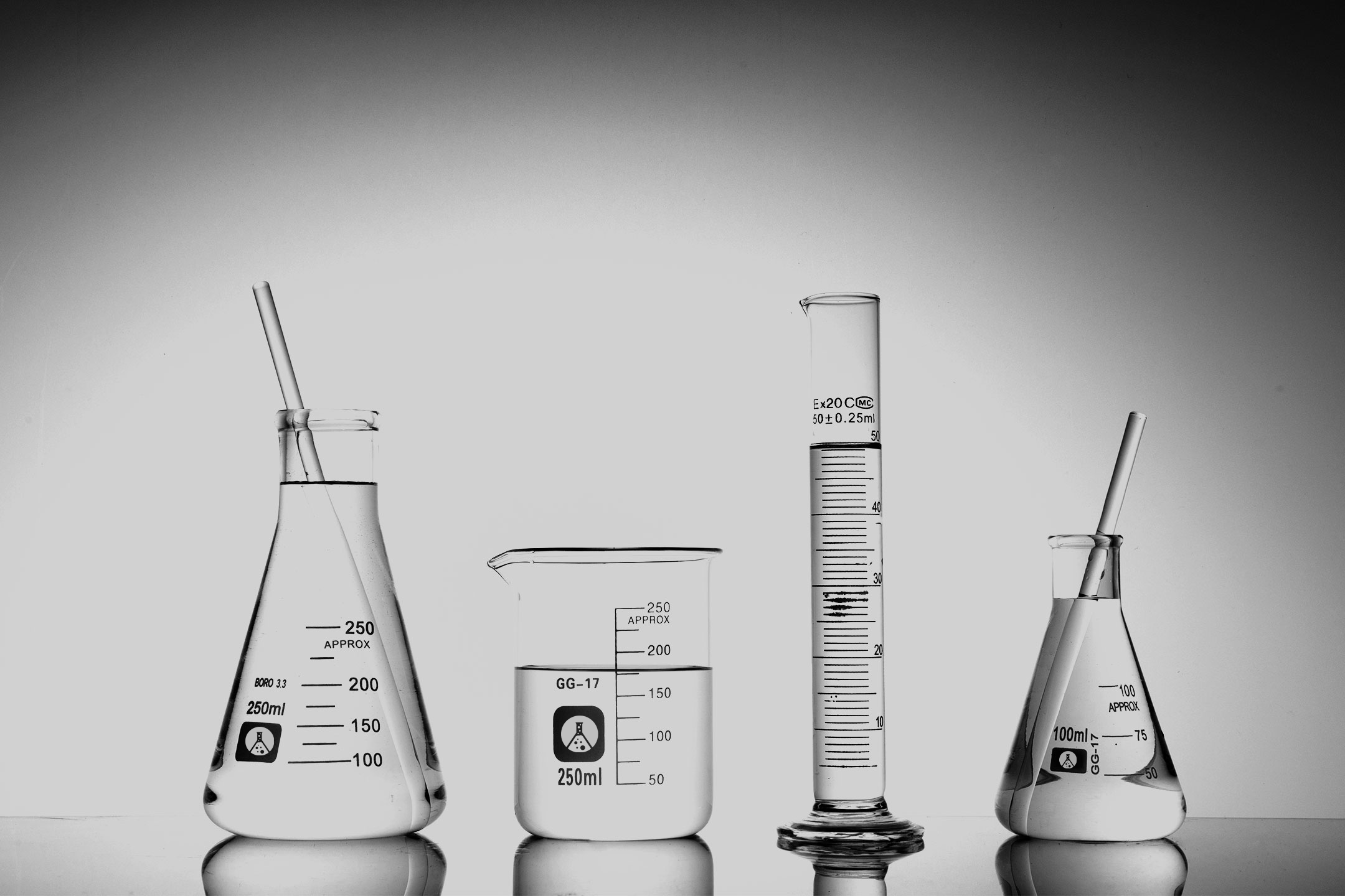 Four laboratory glass beakers and graduated cylinders filled with liquid, with stirring rods inside, arranged in a row against a plain background.