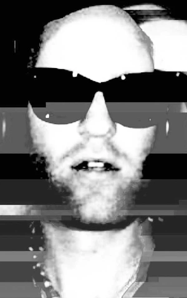 Black-and-white photo of a person's face with short hair and beard wearing sunglasses, image appears distorted with horizontal glitch lines.