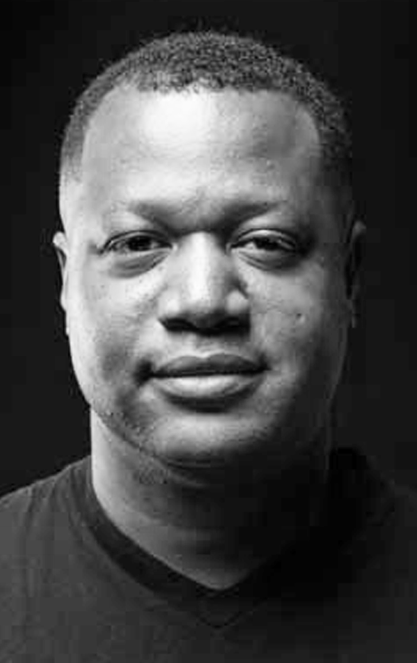 Close-up black and white portrait of a smiling man with short hair and a dark shirt.