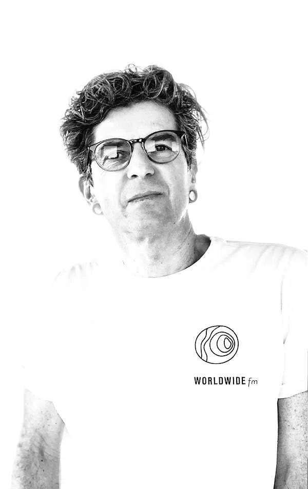 Black and white photo of a person wearing glasses and a white T-shirt with a logo and text reading "WORLDWIDE fm."