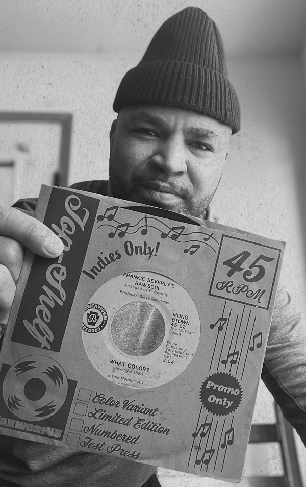 Man wearing a beanie hat holding a record sleeve for Frankie Beverly's 'Raw Soul,' with black and white musical graphics and text.