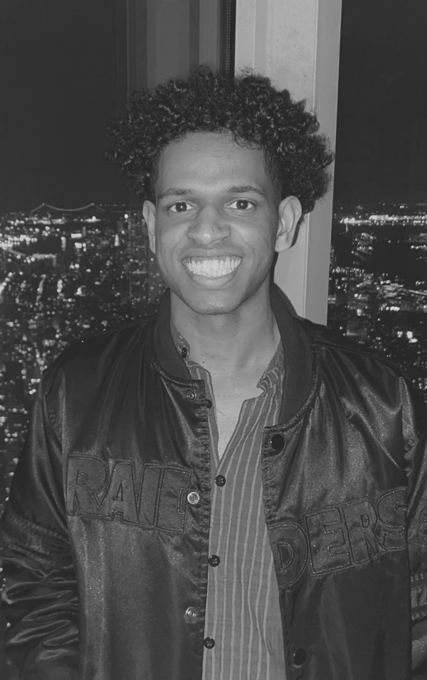 A man with curly hair smiling at night with city lights in the background.