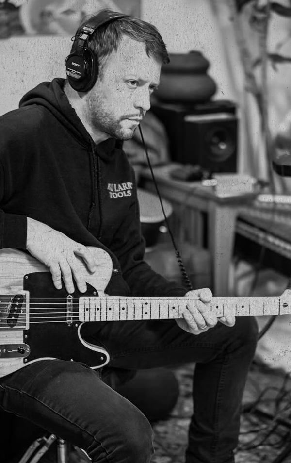 A man wearing headphones playing an electric guitar in a music studio.
