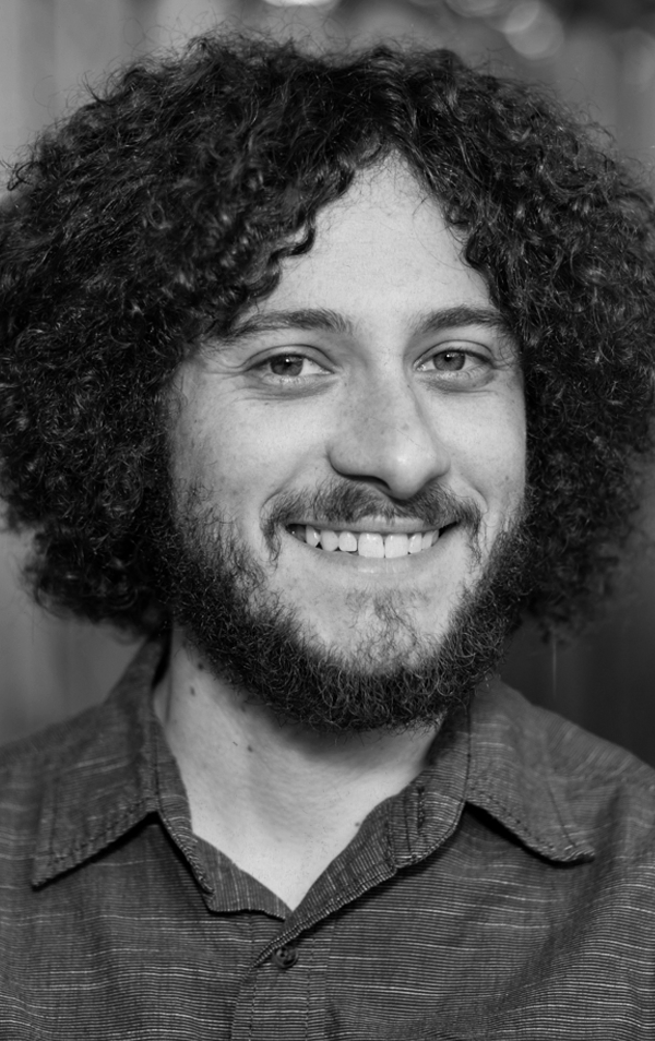 Black and white portrait of a smiling man with curly hair and a beard, wearing a collared shirt.