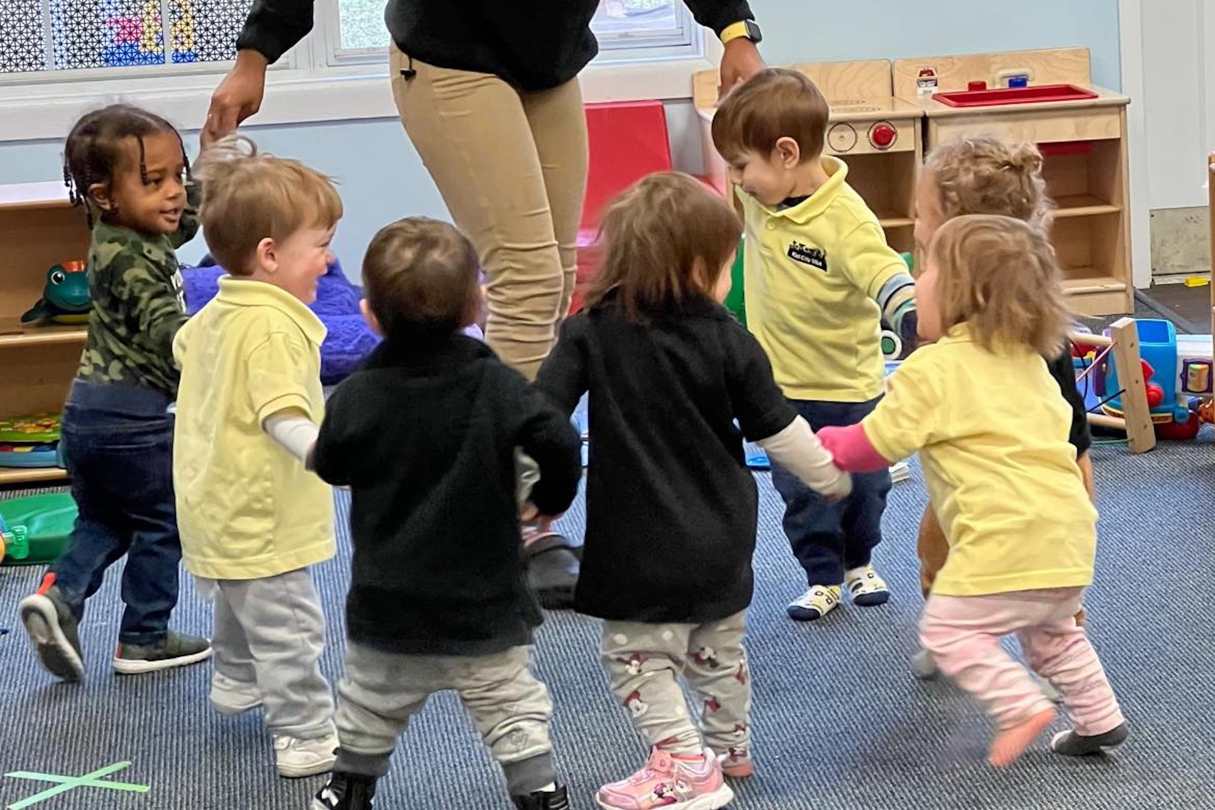 Children playing in a circle with a teacher in a classroom.