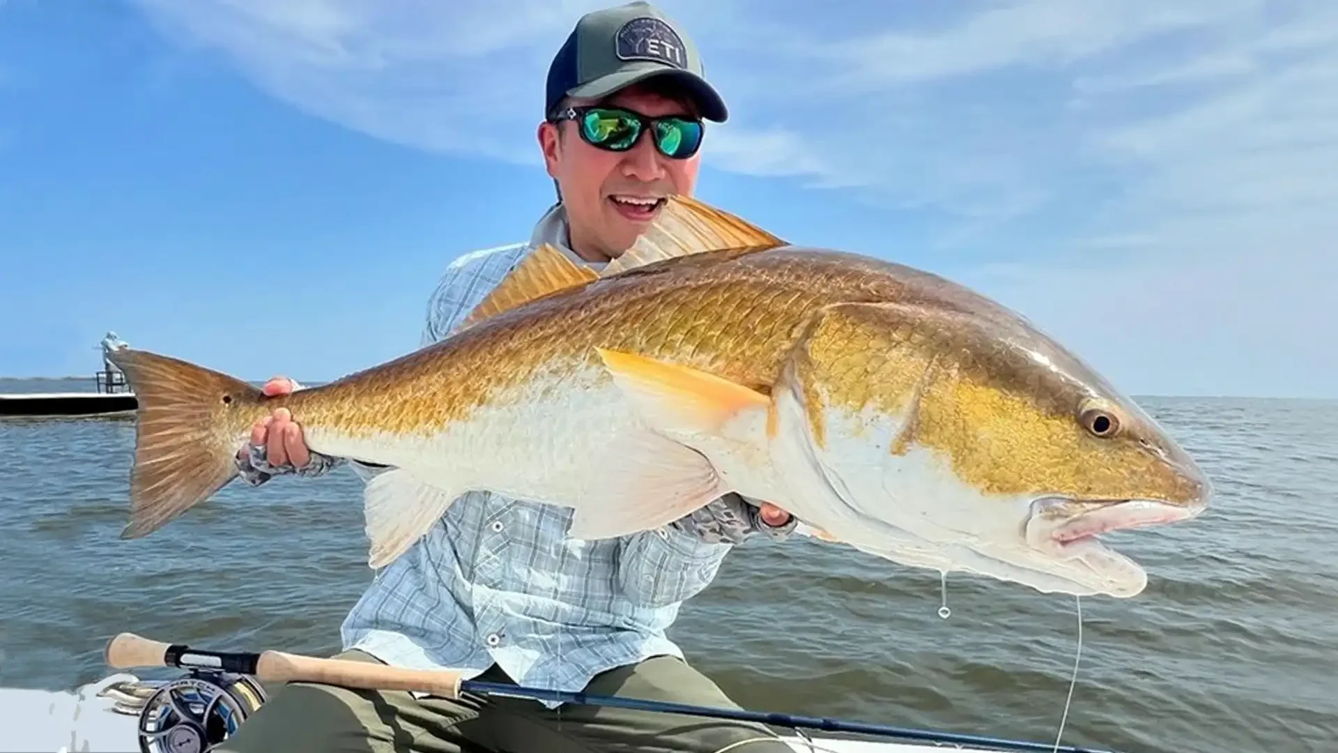 Smiling angler proudly holds a massive redfish caught on a fly rod in the Louisiana saltwater flats.