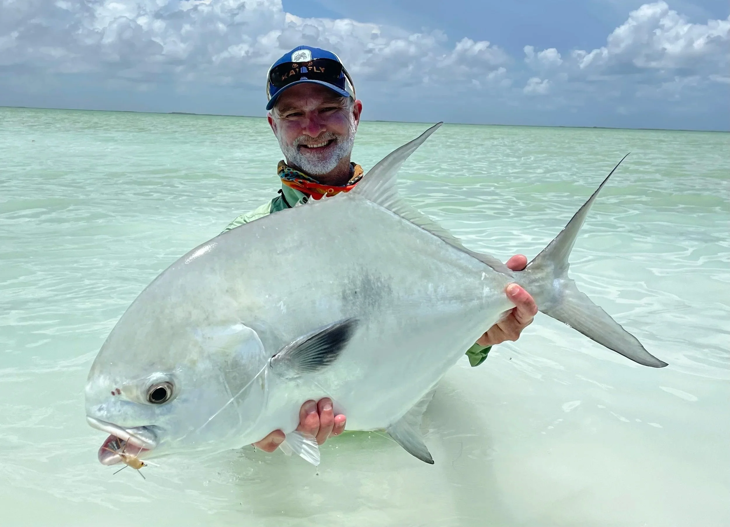 Angler in a blue hat displaying a very large permit in the clear waters of Ascension Bay while fishing with Kāy Fly Lodge