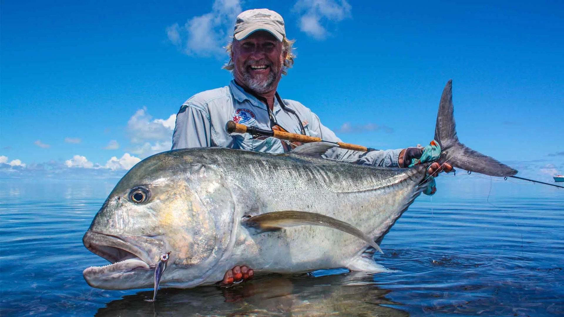 angler standing in waters of alphonse island holding giant trevally