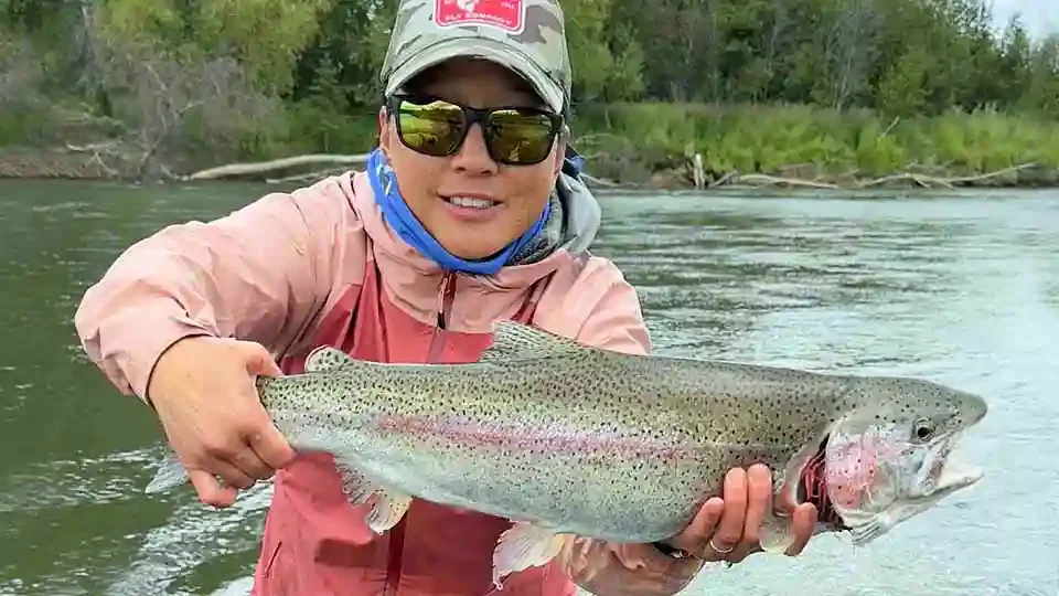 Female angler holding a trophy rainbow trout caught on the Aniak River in Alaska with assistance from a guide at Aniak River Lodge.