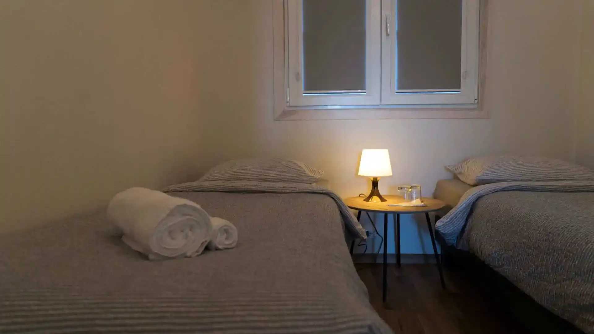 Cozy twin bedroom in an Icelandic Highland fishing lodge, featuring two single beds, a bedside table with a lamp, and a window.