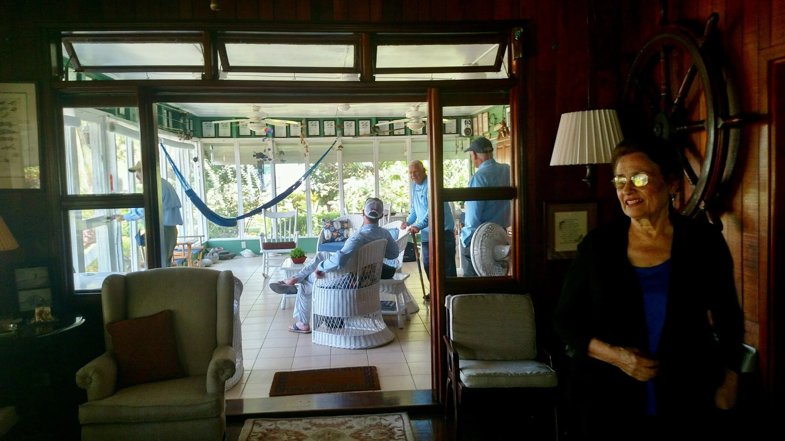 Guests relaxing in the bright, tropical sunroom of Belize River Lodge, with lush greenery visible and a woman smiling indoors.