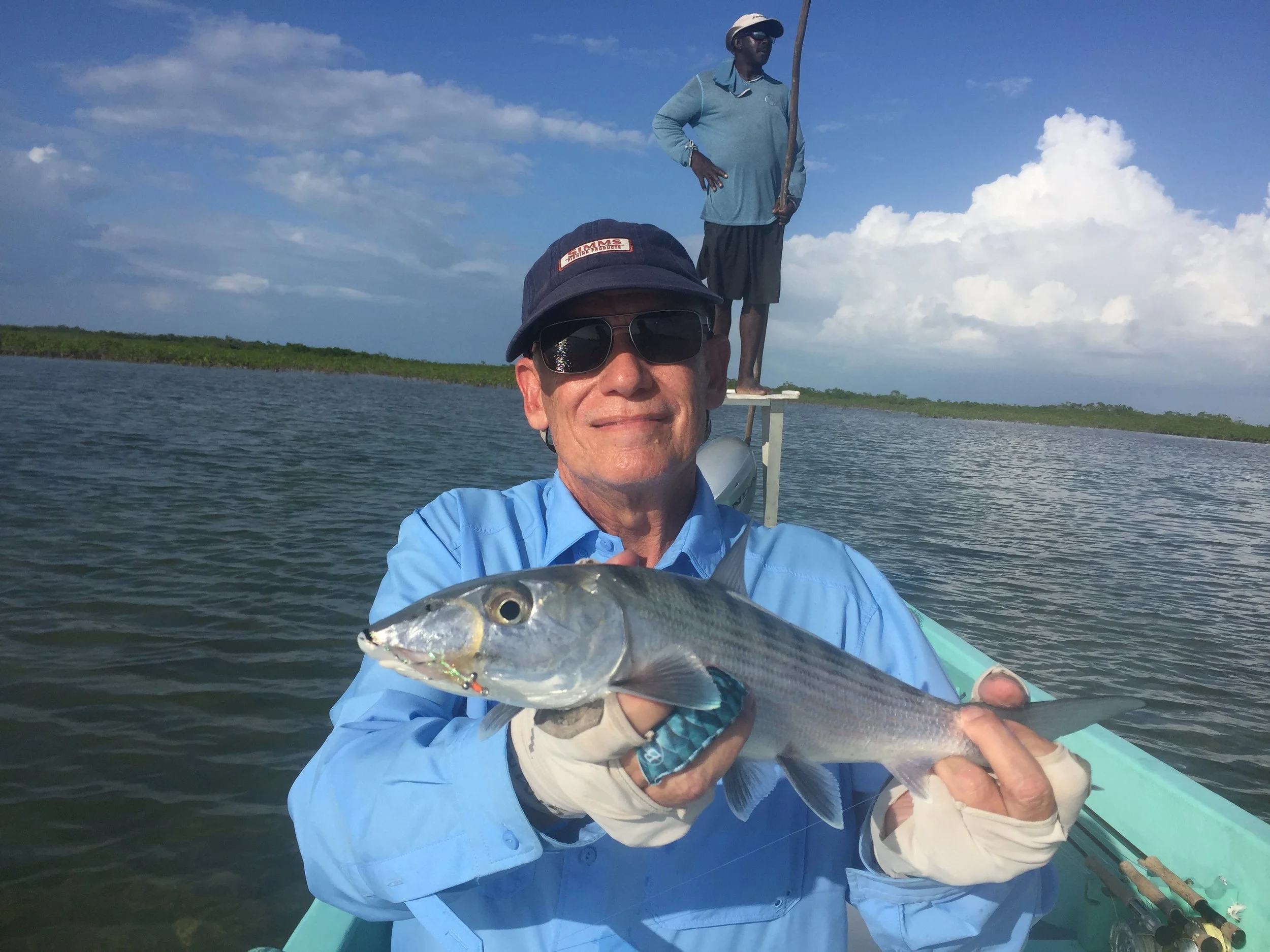 Angler holding a bonefish caught on the flats near Belize River Lodge, with a guide poling the boat in the background.