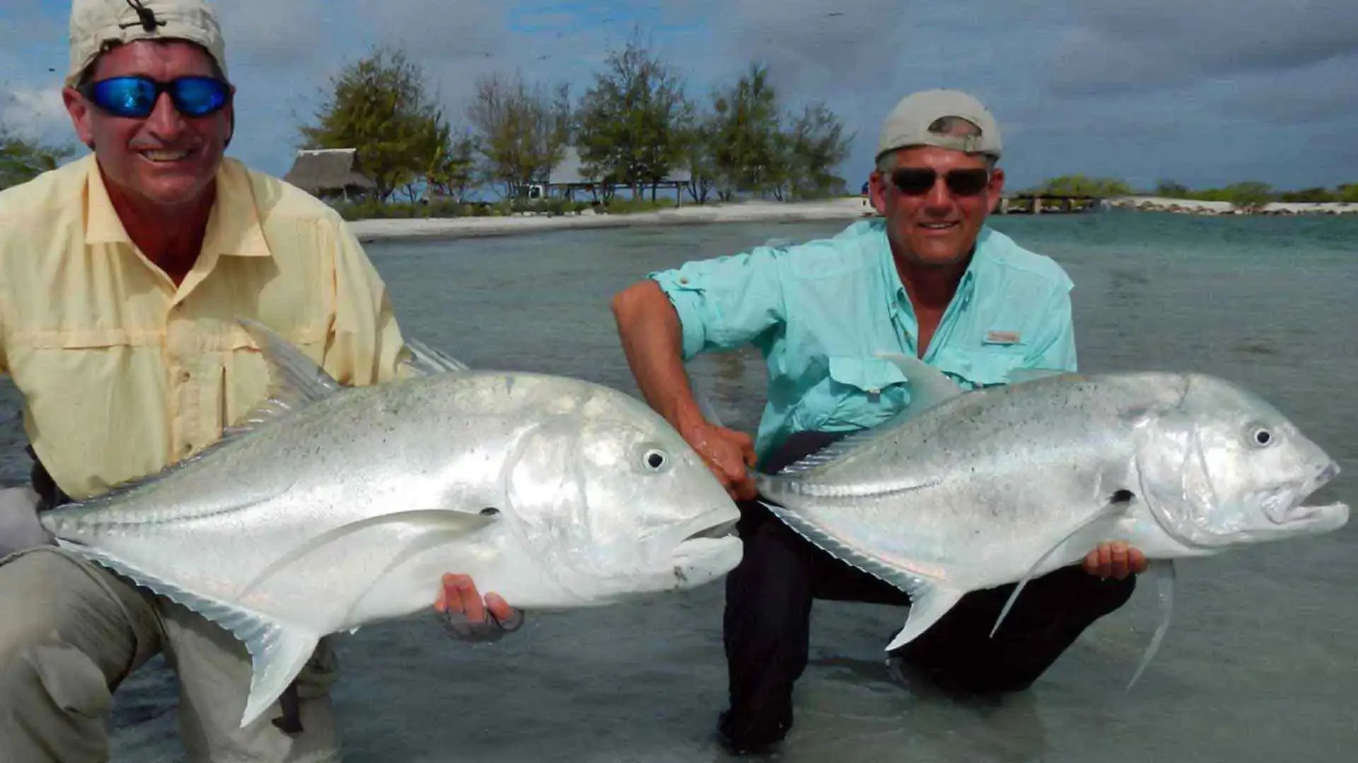 Two anglers standing in shallow water holding giant trevally caught while fishing with The Villages on Christmas Island